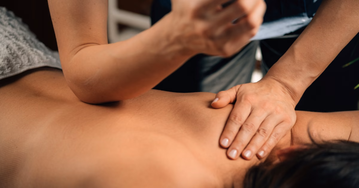 A therapist using firm forearm and hand pressure on the upper back and shoulders to release muscle knots during a massage in Bangkok