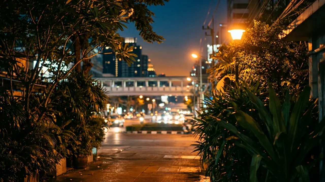 A quiet leafy street near the Asok crossing in Bangkok at night, warm city lights and soft lamplight