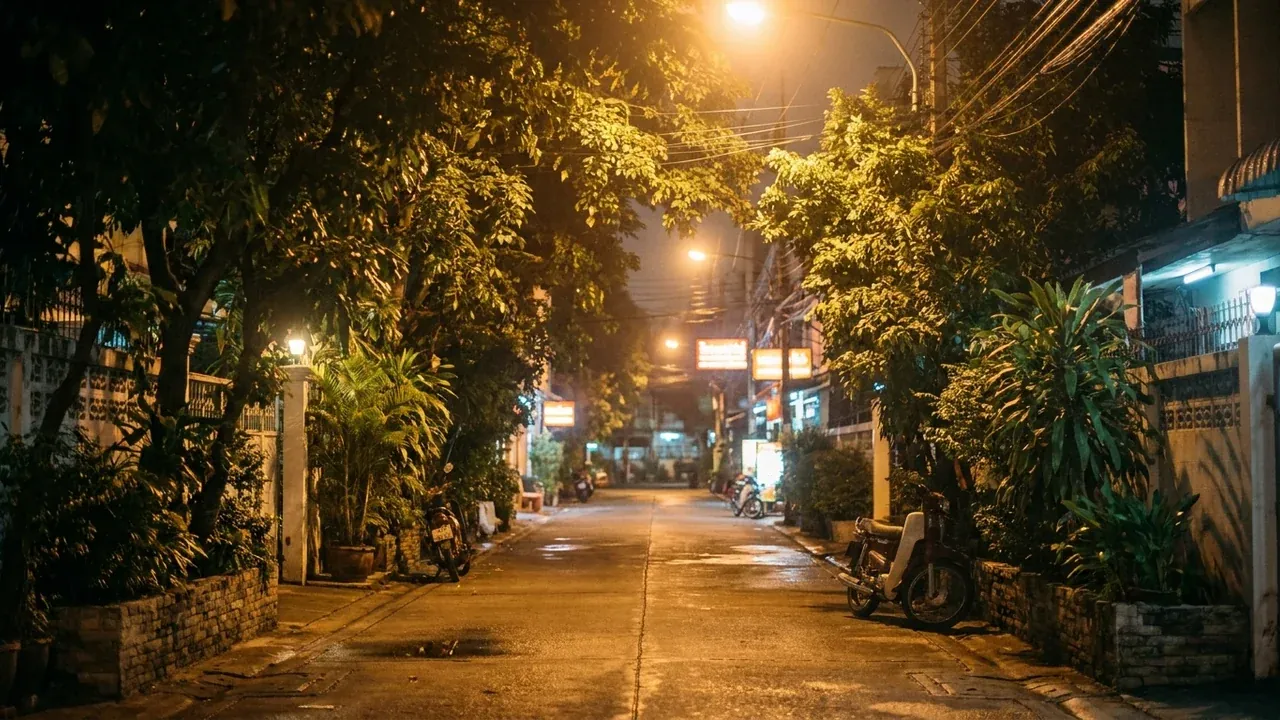A quiet street near Sala Daeng in Silom at night, warm lamplight on the pavement